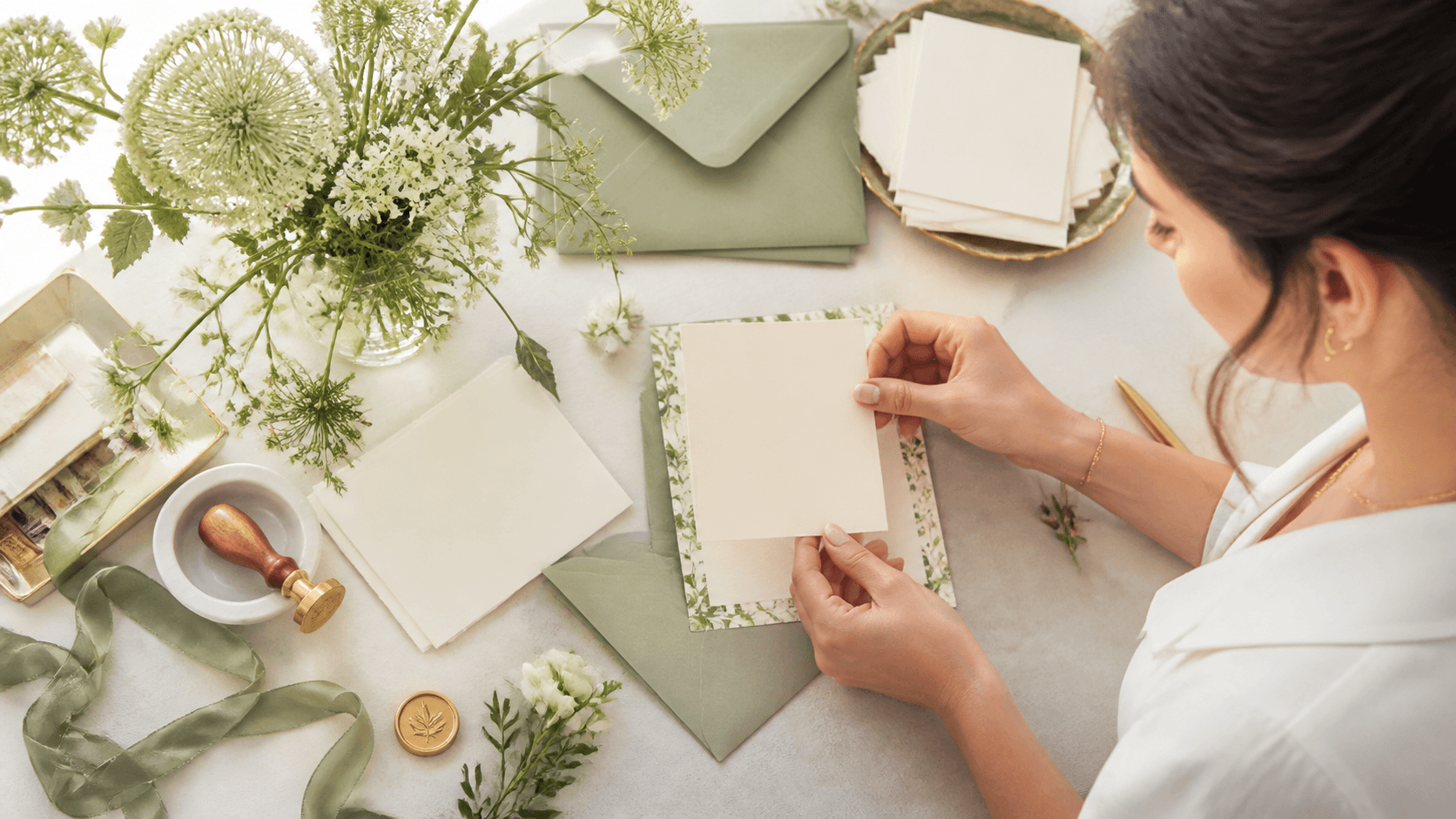 Elegant wedding invitation suite with cream inserts, blush flowers, and gold accents on a white table.